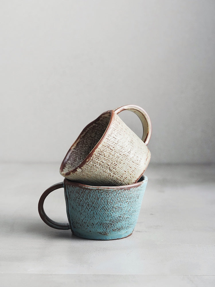 Two ceramic cup stacked on a light gray surface with a neutral background